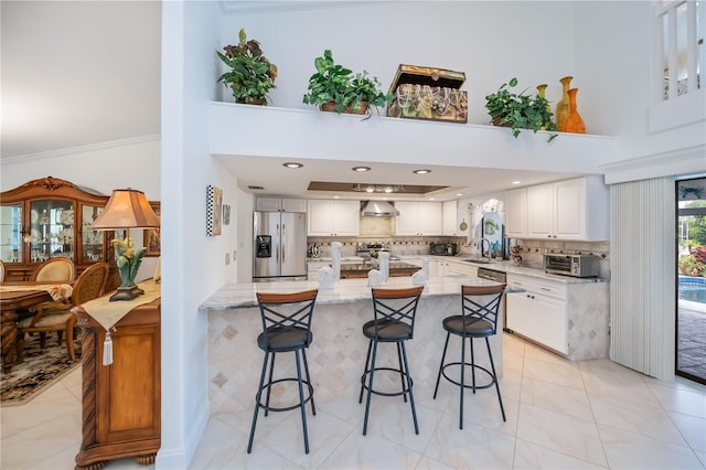 1418 Grebe Dr, Punta Gorda, FL 33950 - kitchen featuring appliances with stainless steel finishes, a kitchen bar, wall chimney range hood, decorative backsplash, and white cabinetry