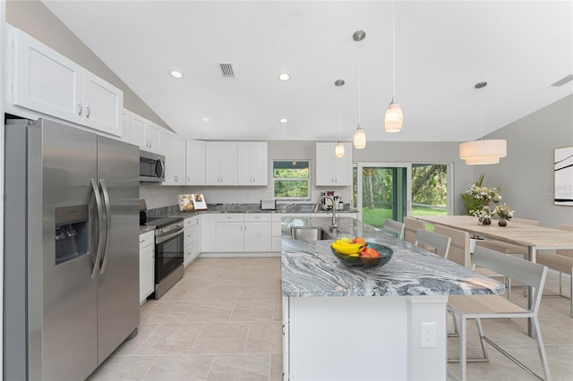 4863 Las Almanos Ave, North Port, FL 34288 - kitchen with appliances with stainless steel finishes, vaulted ceiling, light stone counters, white cabinetry, and a kitchen island with sink