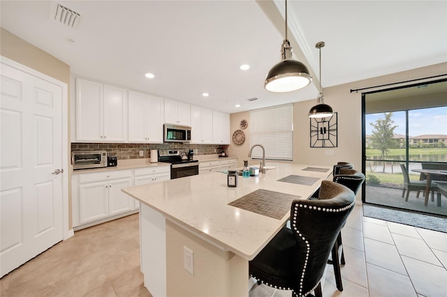12425 Ghiberti Cir Unit 101, Venice, FL 34293 - kitchen featuring appliances with stainless steel finishes, tasteful backsplash, light tile patterned flooring, white cabinetry, and a breakfast bar