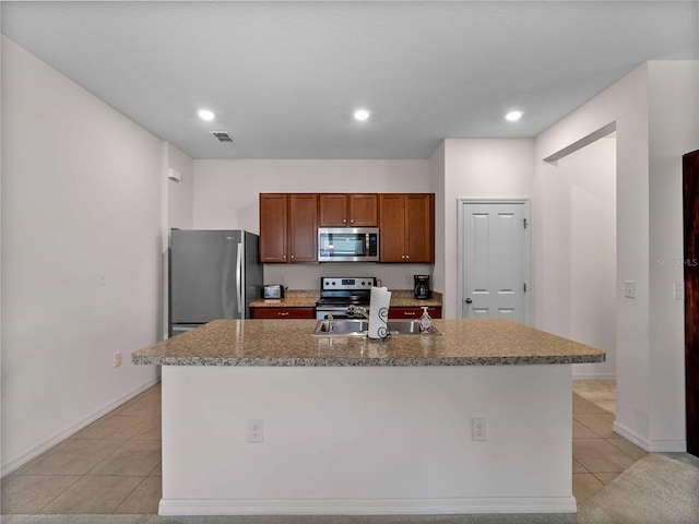 8814 Tuscany Isles Dr, Punta Gorda, FL 33950 - kitchen with stainless steel appliances, light tile patterned floors, a kitchen island with sink, brown cabinets, and recessed lighting
