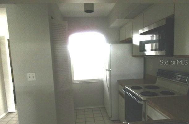 429 Cerromar Ln Unit 353, Venice, FL 34293 - kitchen with white range with electric cooktop, stainless steel microwave, light tile patterned floors, and white cabinets