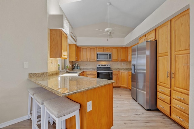 2474 Rio De Janeiro Ave, Punta Gorda, FL 33983 - kitchen featuring appliances with stainless steel finishes, a peninsula, light stone counters, light wood finished floors, and a kitchen breakfast bar