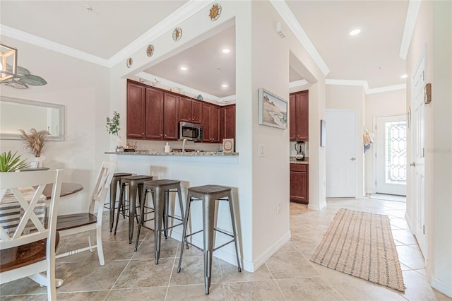 20333 Lagente Cir, Venice, FL 34293 - kitchen with stainless steel microwave, a breakfast bar area, ornamental molding, light tile patterned floors, and a peninsula