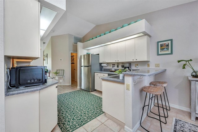 860 Silver Springs Ter NW, Port Charlotte, FL 33948 - kitchen with freestanding refrigerator, a peninsula, a kitchen bar, light tile patterned floors, and white cabinetry