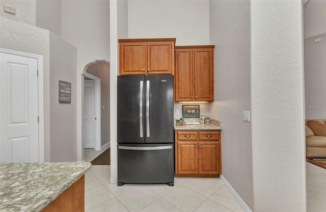 771 Rotonda Cir, Rotonda West, FL 33947 - kitchen with freestanding refrigerator, light tile patterned floors, light stone counters, brown cabinets, and a textured wall