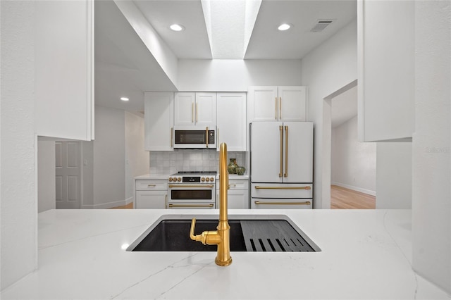 25451 Kowloon Ln, Punta Gorda, FL 33983 - kitchen with high quality appliances, white cabinets, decorative backsplash, recessed lighting, and wood finished floors
