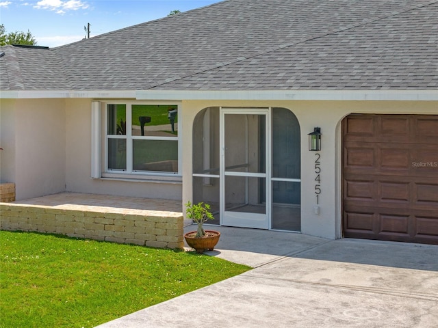 25451 Kowloon Ln, Punta Gorda, FL 33983 - view of exterior entry with a shingled roof, stucco siding, an attached garage, and a yard