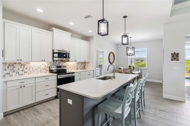 13416 Trascoro Ln, Port Charlotte, FL 33981 - kitchen featuring appliances with stainless steel finishes, decorative backsplash, a kitchen island with sink, recessed lighting, and white cabinetry