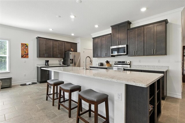 2456 Nabble Ln, North Port, FL 34288 - kitchen featuring appliances with stainless steel finishes, crown molding, dark brown cabinets, a breakfast bar area, and an island with sink