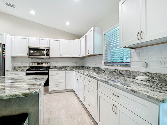 5493 Jody Ave, North Port, FL 34288 - kitchen with appliances with stainless steel finishes, vaulted ceiling, light stone countertops, light marble finish floors, and white cabinets