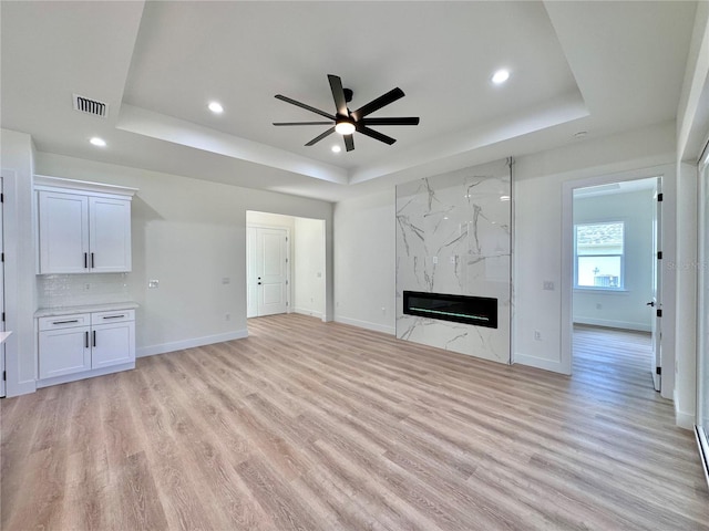 4748 Sylvania Ave, North Port, FL 34286 - unfurnished living room featuring a tray ceiling, a ceiling fan, light wood-style flooring, recessed lighting, and a high end fireplace