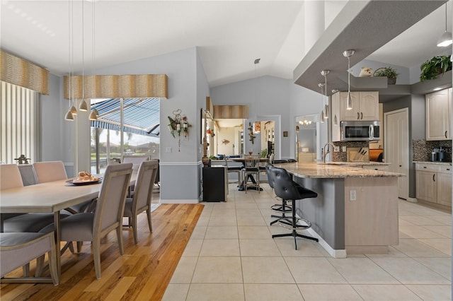 1422 Via Milanese, Punta Gorda, FL 33950 - kitchen featuring stainless steel microwave, decorative backsplash, an island with sink, a kitchen breakfast bar, and light stone countertops