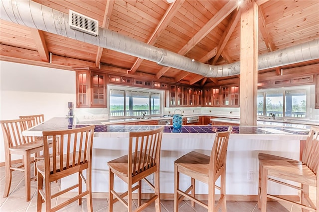 kitchen featuring tile countertops, wooden ceiling, a kitchen breakfast bar, and light tile patterned floors