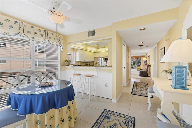 interior space featuring kitchen peninsula, light tile flooring, ceiling fan, and a breakfast bar