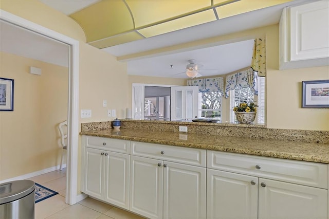 kitchen with light tile floors, white cabinetry, ceiling fan, and light stone countertops