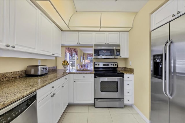 kitchen with white cabinets, light tile flooring, stainless steel appliances, and dark stone countertops