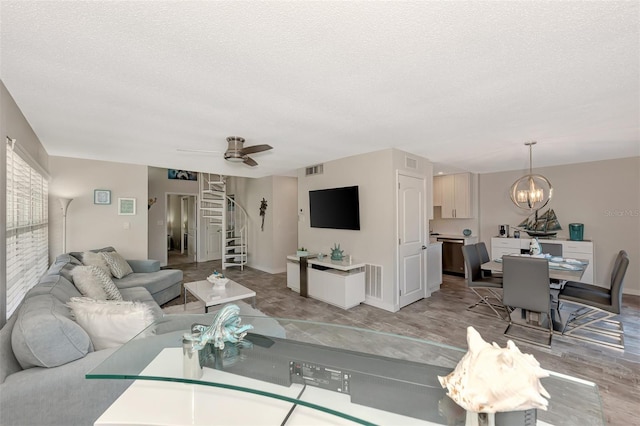 living room with a textured ceiling, ceiling fan with notable chandelier, and light hardwood / wood-style flooring