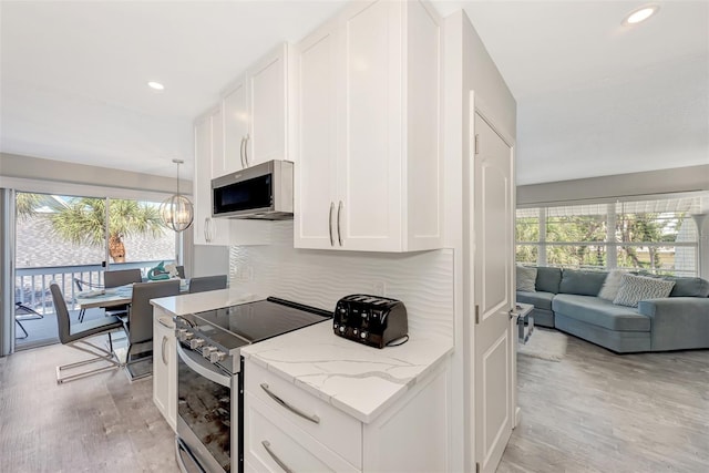 kitchen featuring pendant lighting, white cabinetry, appliances with stainless steel finishes, light wood-type flooring, and light stone counters