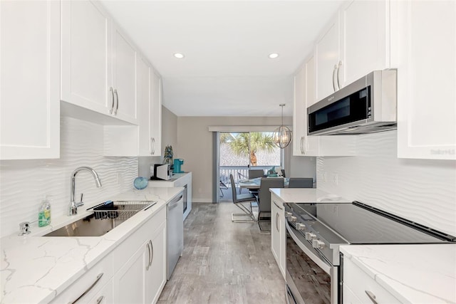 kitchen featuring hanging light fixtures, white cabinets, stainless steel appliances, light stone countertops, and light wood-type flooring