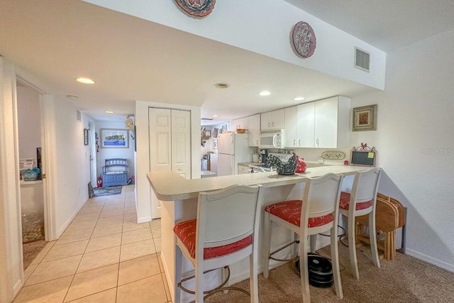 kitchen featuring a kitchen breakfast bar, kitchen peninsula, white appliances, and light tile floors