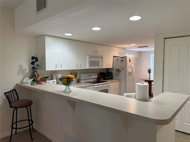 kitchen with kitchen peninsula, white appliances, light tile floors, white cabinets, and a kitchen bar