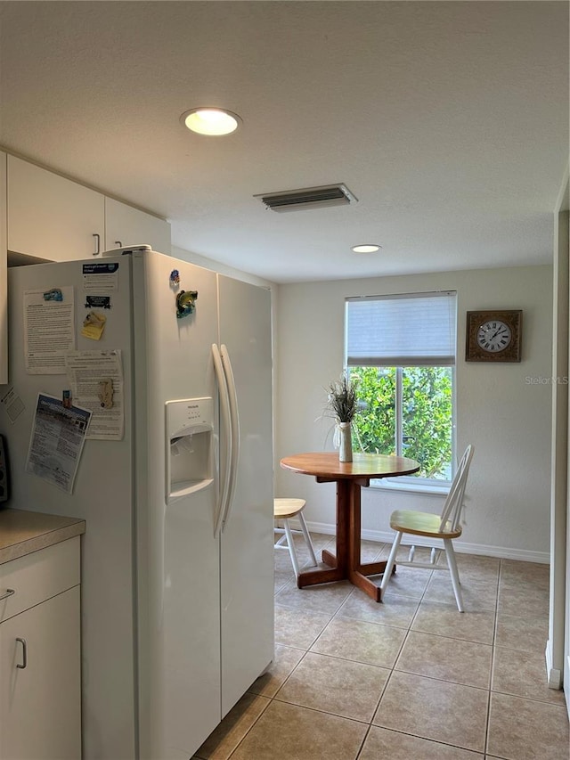 kitchen with white cabinets, white fridge with ice dispenser, and light tile flooring