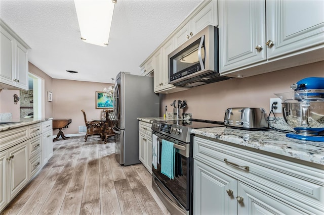 kitchen with light stone countertops, stainless steel appliances, light hardwood / wood-style flooring, and white cabinets