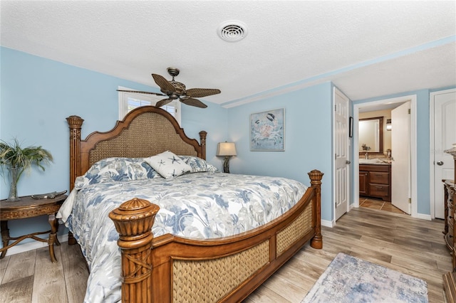 bedroom with ceiling fan, ensuite bathroom, a textured ceiling, and light wood-type flooring