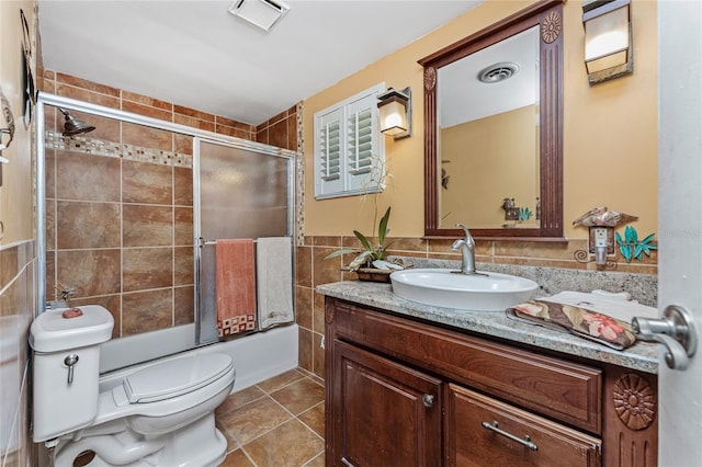 full bathroom with vanity, tile patterned floors, combined bath / shower with glass door, toilet, and tile walls