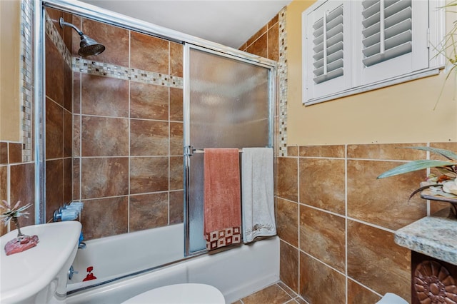 bathroom with tile patterned floors, toilet, shower / bath combination with glass door, and tile walls