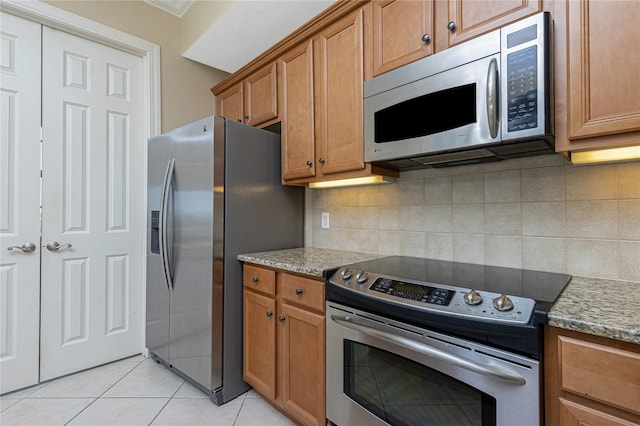 kitchen featuring tasteful backsplash, stainless steel appliances, light tile flooring, and light stone countertops