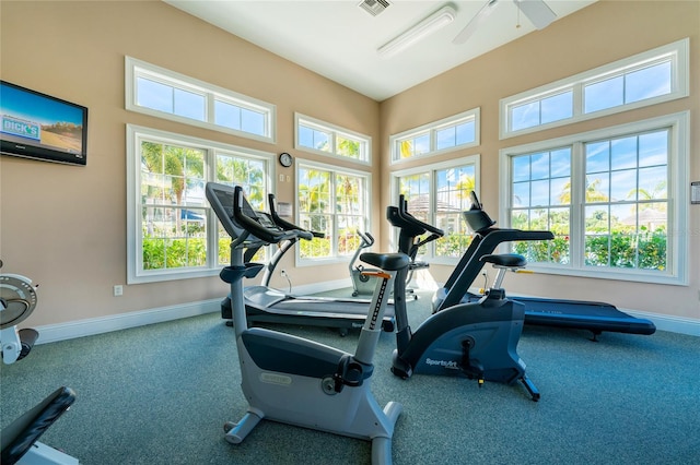 gym with a healthy amount of sunlight, ceiling fan, and dark carpet