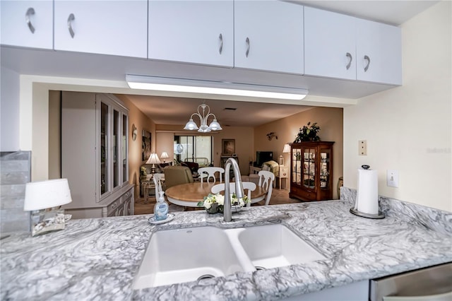 kitchen featuring a notable chandelier, white cabinets, hanging light fixtures, light stone counters, and sink