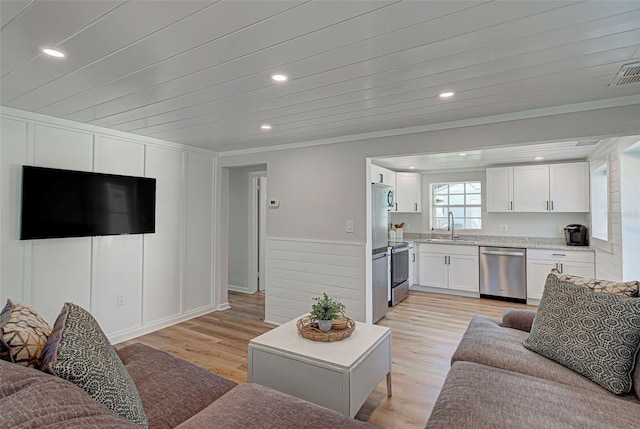 living room with ornamental molding, sink, and light wood-type flooring