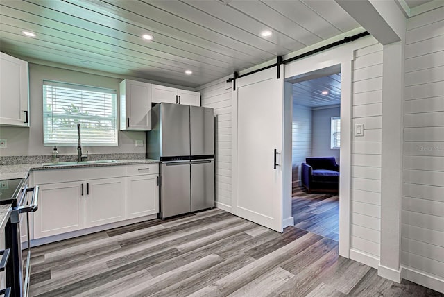 kitchen featuring sink, appliances with stainless steel finishes, light hardwood / wood-style floors, a barn door, and white cabinetry