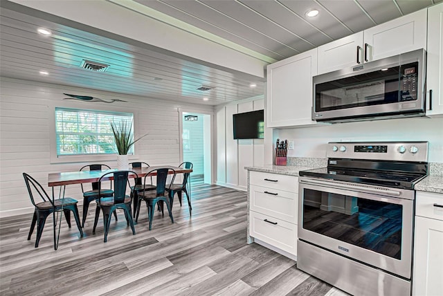 kitchen featuring light stone counters, white cabinetry, appliances with stainless steel finishes, and light wood-type flooring