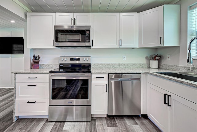 kitchen with light hardwood / wood-style floors, light stone countertops, stainless steel appliances, and white cabinetry