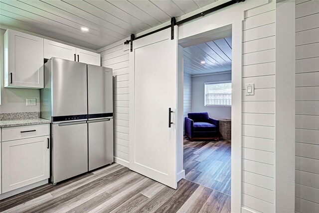 kitchen with a barn door, white cabinets, light hardwood / wood-style floors, and stainless steel refrigerator