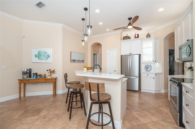 kitchen featuring ceiling fan, a kitchen breakfast bar, hanging light fixtures, stainless steel appliances, and white cabinetry