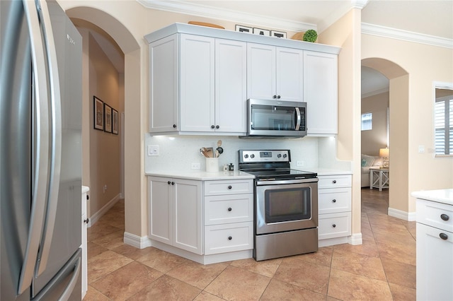 kitchen with ornamental molding, appliances with stainless steel finishes, backsplash, light tile flooring, and white cabinetry