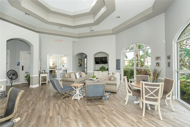 living room with light hardwood / wood-style flooring, plenty of natural light, a high ceiling, and french doors