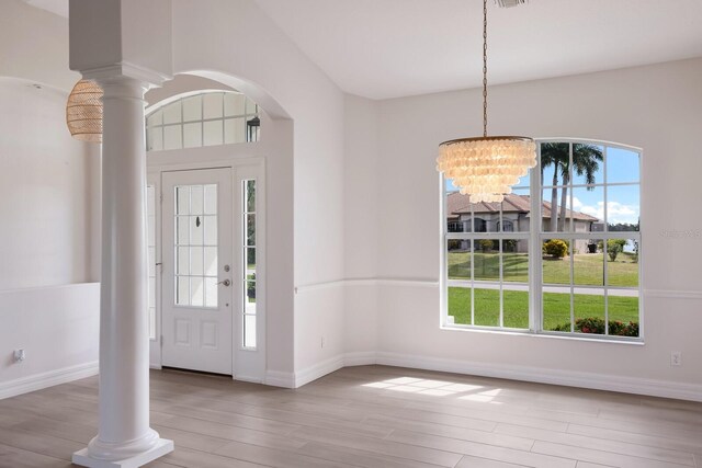 foyer with light hardwood / wood-style flooring, an inviting chandelier, plenty of natural light, and ornate columns