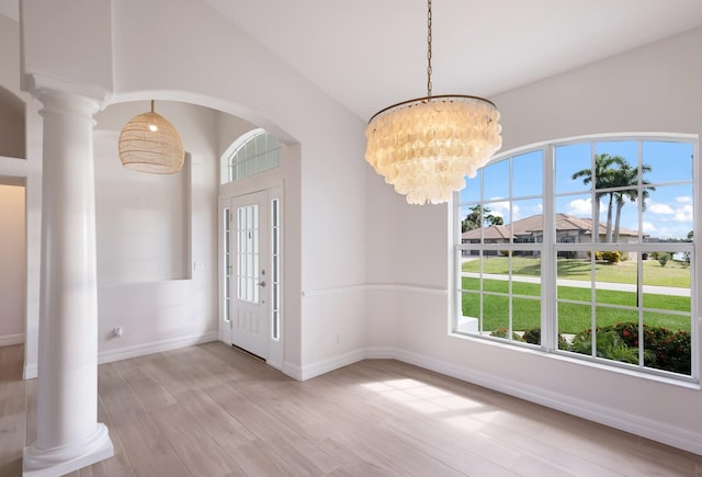 foyer entrance with ornate columns, light hardwood / wood-style flooring, and an inviting chandelier