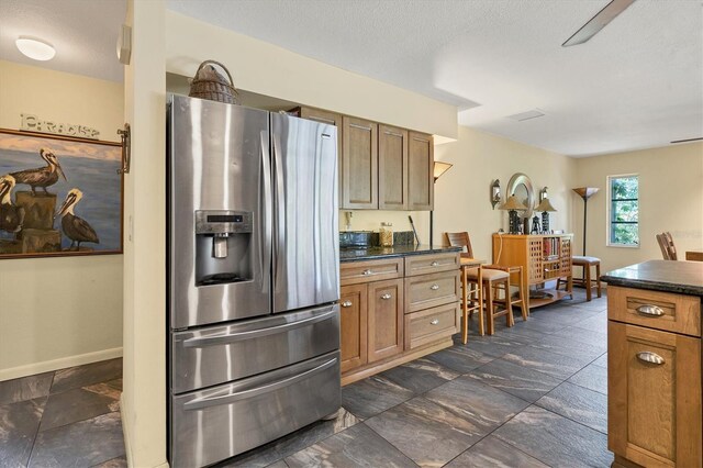 kitchen with stainless steel fridge with ice dispenser, dark tile flooring, and a textured ceiling