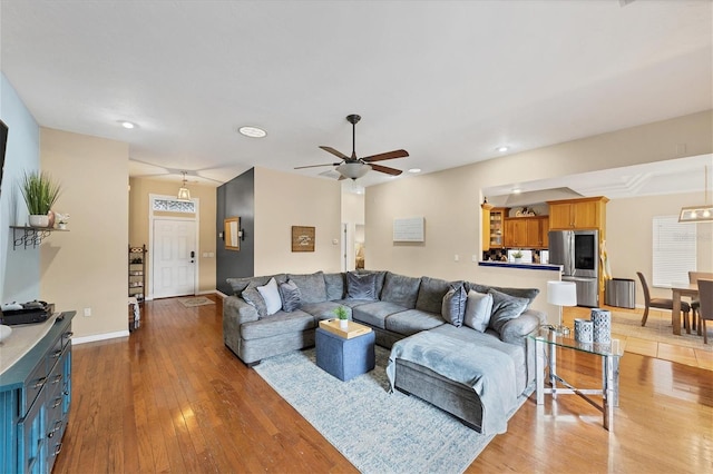 living area with baseboards, ceiling fan, and light wood finished floors