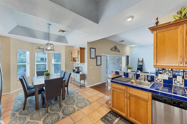 kitchen with light tile patterned floors, visible vents, tile counters, dishwasher, and a tray ceiling