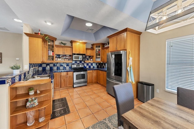 kitchen with dark countertops, glass insert cabinets, appliances with stainless steel finishes, a tray ceiling, and open shelves