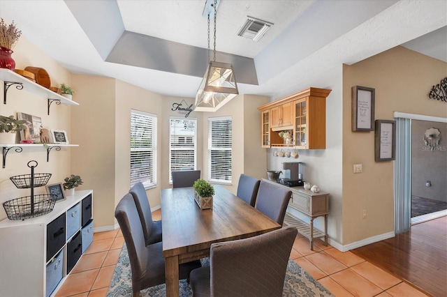 dining room featuring light tile patterned flooring, a raised ceiling, visible vents, and baseboards