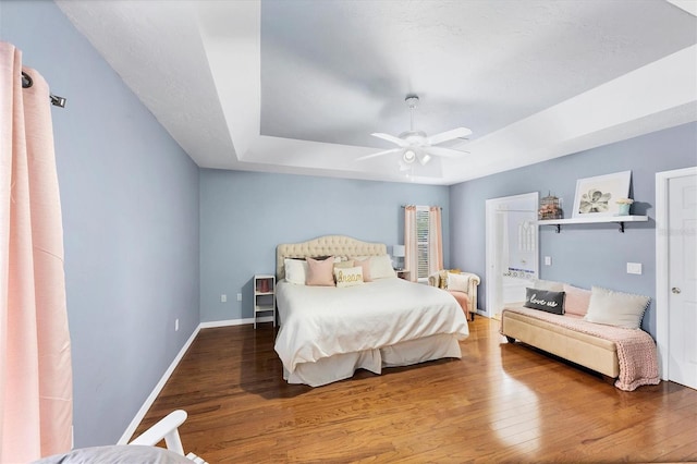 bedroom featuring a tray ceiling, wood finished floors, a ceiling fan, and baseboards