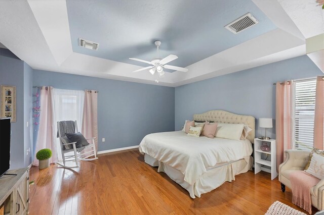 bedroom featuring light wood finished floors, visible vents, a tray ceiling, and baseboards